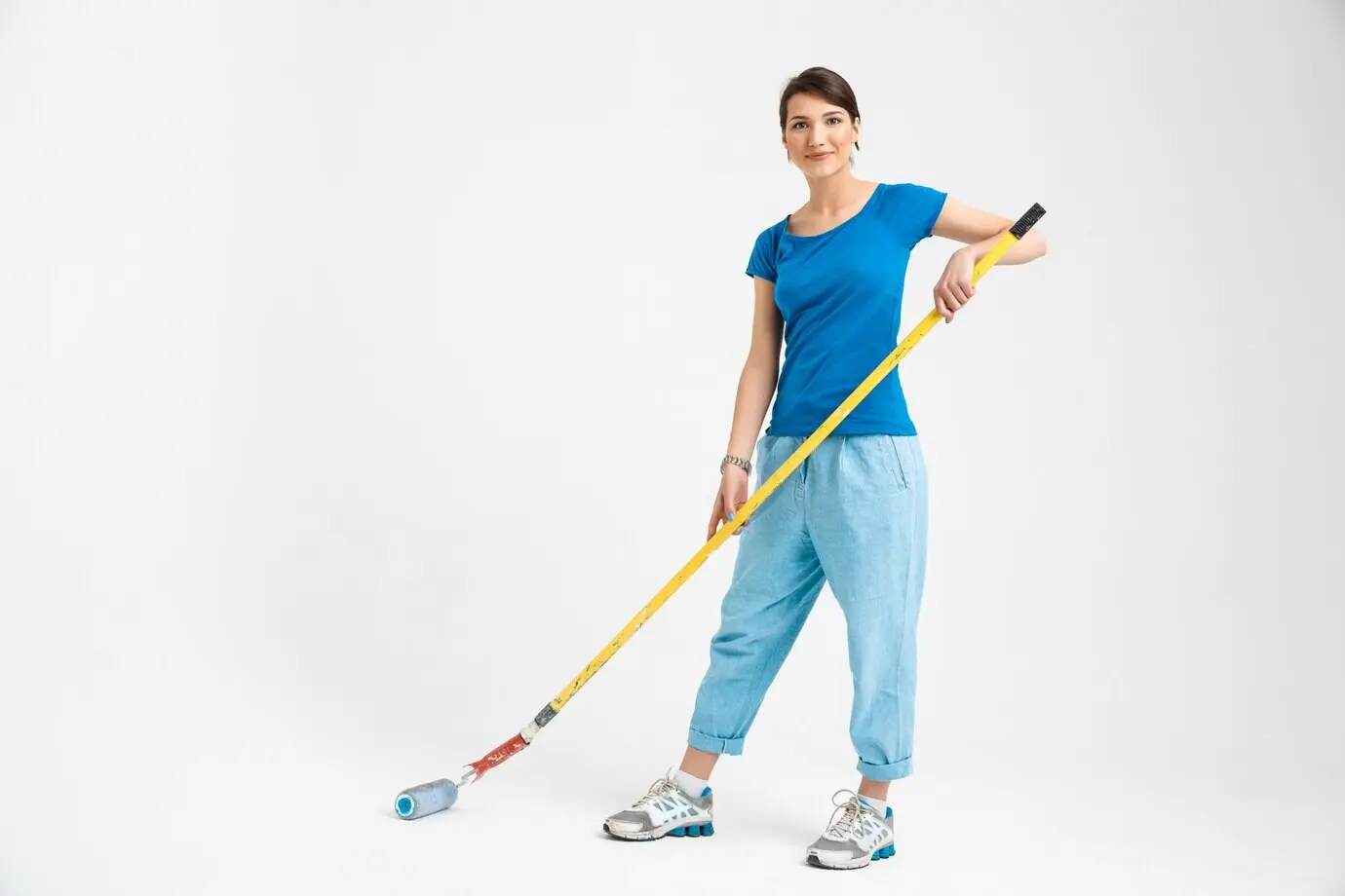 Hübsche junge Frau repariert ein Zimmer und hält eine Farbrolle.